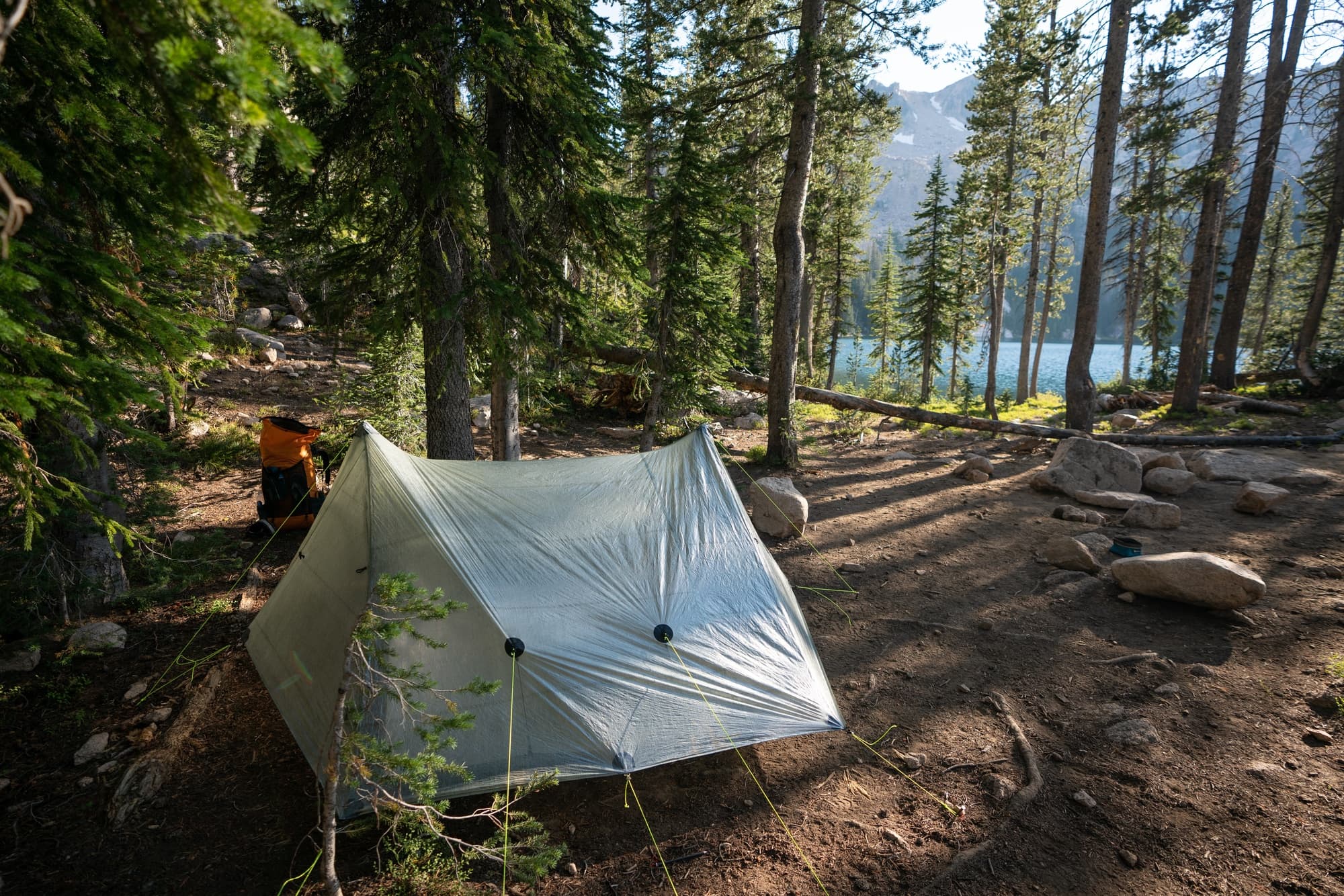 A tent pitched in a legal campsite in the Sawtooth mountains in Idaho with trees, dirt, and rocks surrounding the tent.