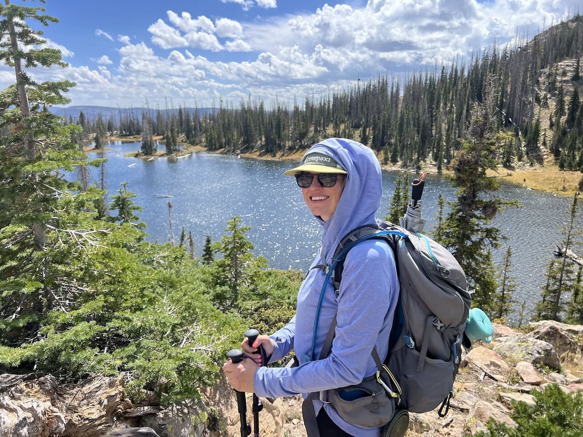 Kristen Bor hiking in the Uintas. She's wearing a sun hoody and there is a mountain lake in the background